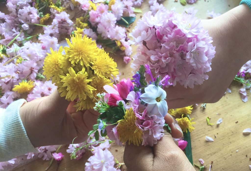 写真：レイ作りのための花を持つ、三人の子どもの手